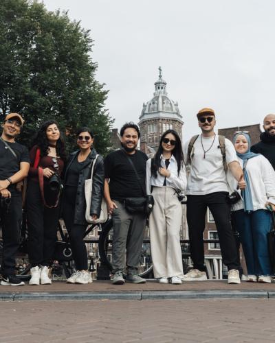 A joyful group of tourists posing in front of a scenic Amsterdam background, capturing the essence of travel and urban exploration.