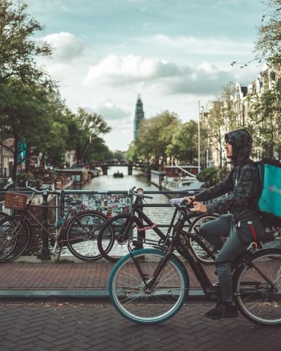 Food delivery cyclist rides through Amsterdam, showcasing urban lifestyle and iconic canals.