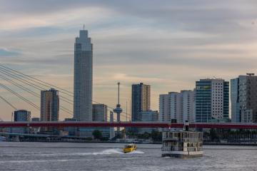 Scenic view of Rotterdam cityscape with boats on calm river at sunset.