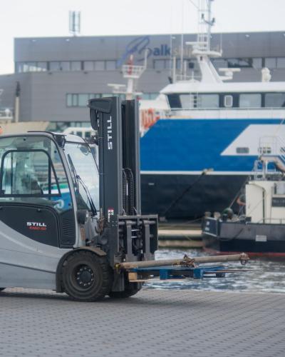 Forklift operating in Urk harbor, Flevoland with ships in the background, urban scenery.