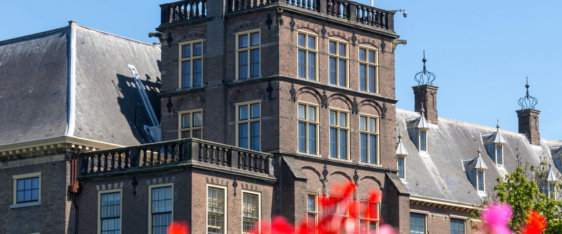 The Dutch Parliament Building stands tall with EU and Dutch flags, vibrant flowers add color.