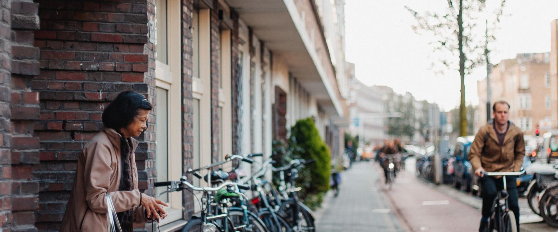 A vibrant street scene in a Dutch neighborhood with people, bicycles, and a small dog.