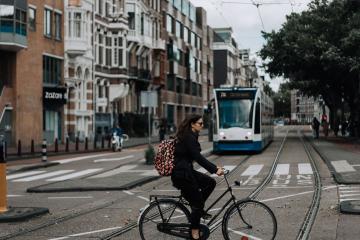 A woman rides a bicycle in Amsterdam with a tram and classic European architecture in view.