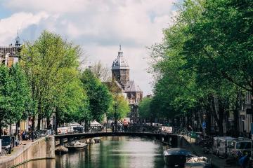 Explore the charming canals and historic architecture of Amsterdam, featuring boats and lush greenery.