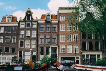 Discover the serene beauty of Amsterdam's iconic canal lined with historic Dutch architecture boats under a clear blue sky.